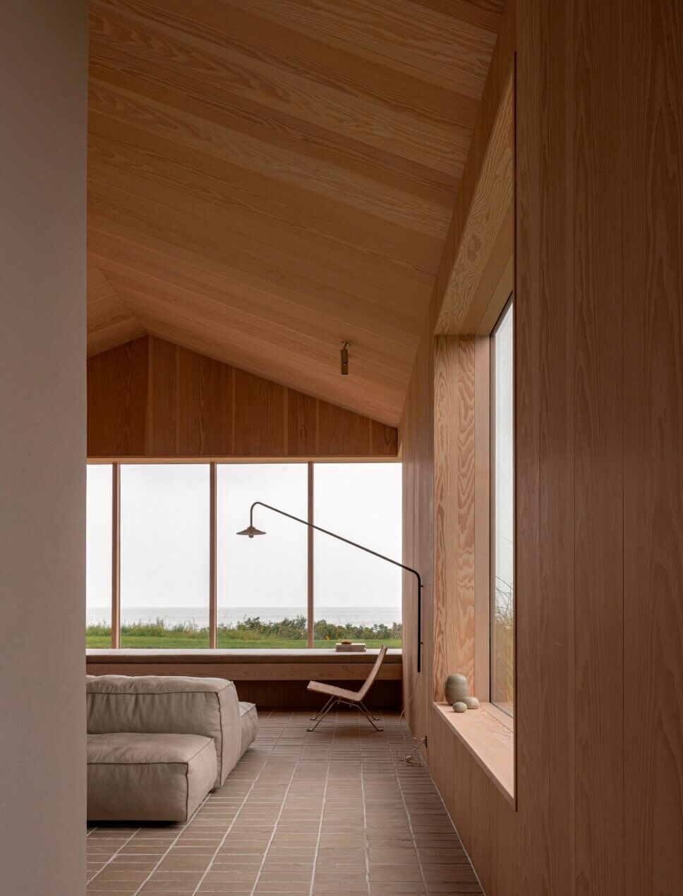 Minimalistisch eingerichtetes, mit Holz vertäfeltes Wohnzimmer in Architektenhaus mit Panoramafenster und Meerblick