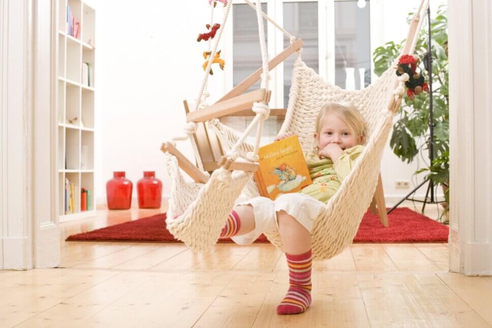 Kind schaukelt in modernem Hängesessel in Wohnzimmer